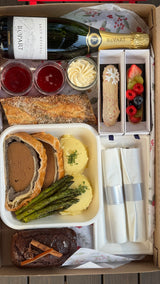 Gourmet food box with a bottle of champagne, pastries, and other treats.
